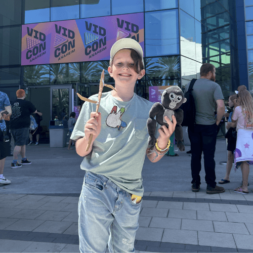 Grinning fan outside Vidcon holding Stick plush and Gorilla Tag Monke plush