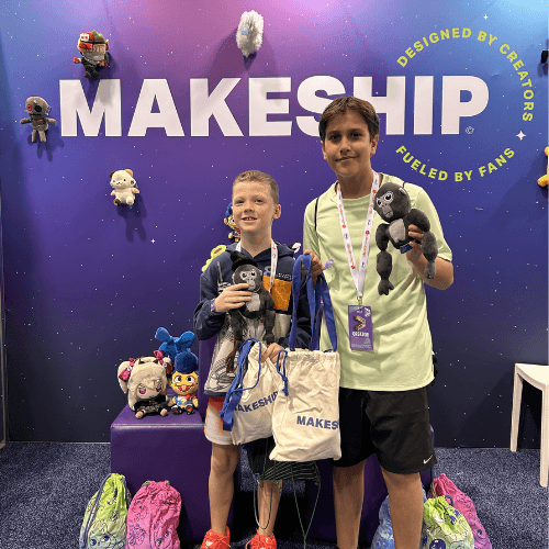 Two fans at the Makeship Vidcon booth smiling and holding Gorilla Tag Monke plushes and Makeship merchandise bags